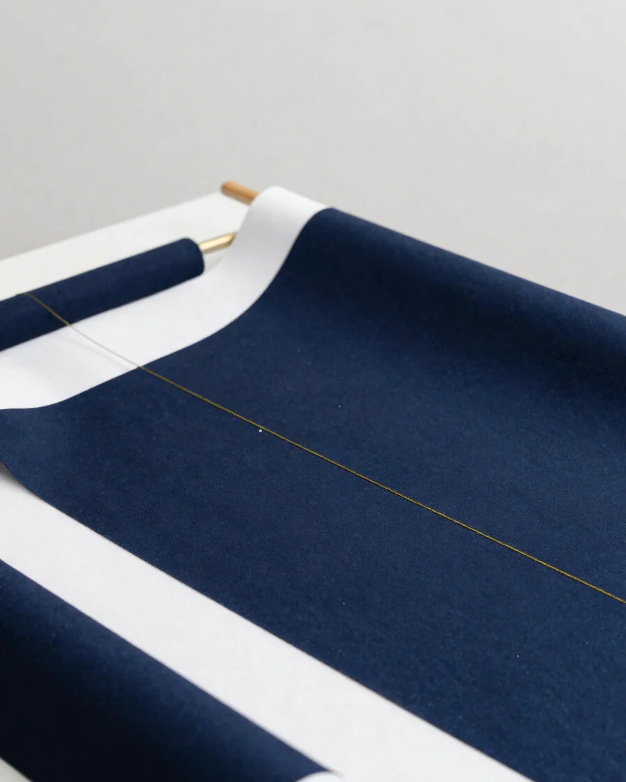 Xưởng may studio trang nhã, bàn cắt vải màu navy và trắng, cận cảnh đường chỉ may vàng nhạt, ánh sáng studio mềm trung t